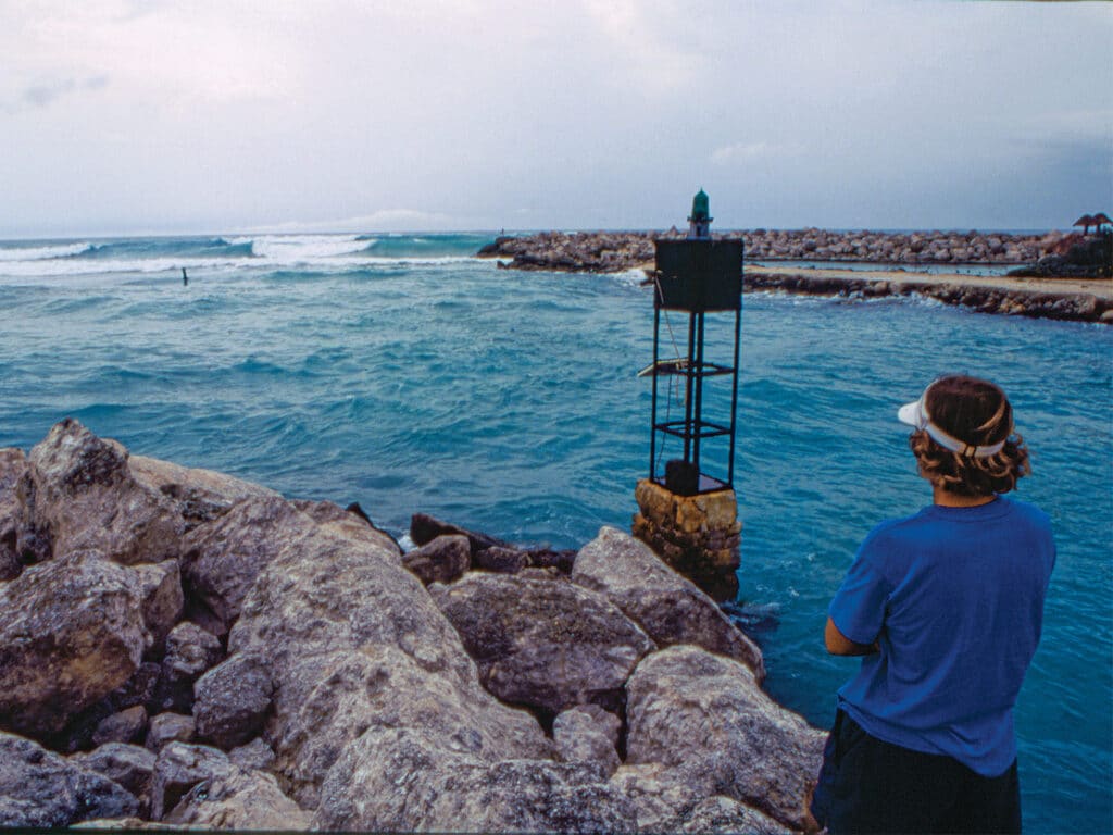 A captain stands on a jetty near the ocean.