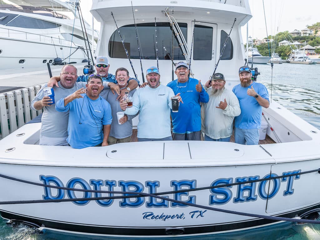 A sport-fishing team stands in the cockpit of a fishing boat and celebrates a win. Double Shot is the name on the boat's transom