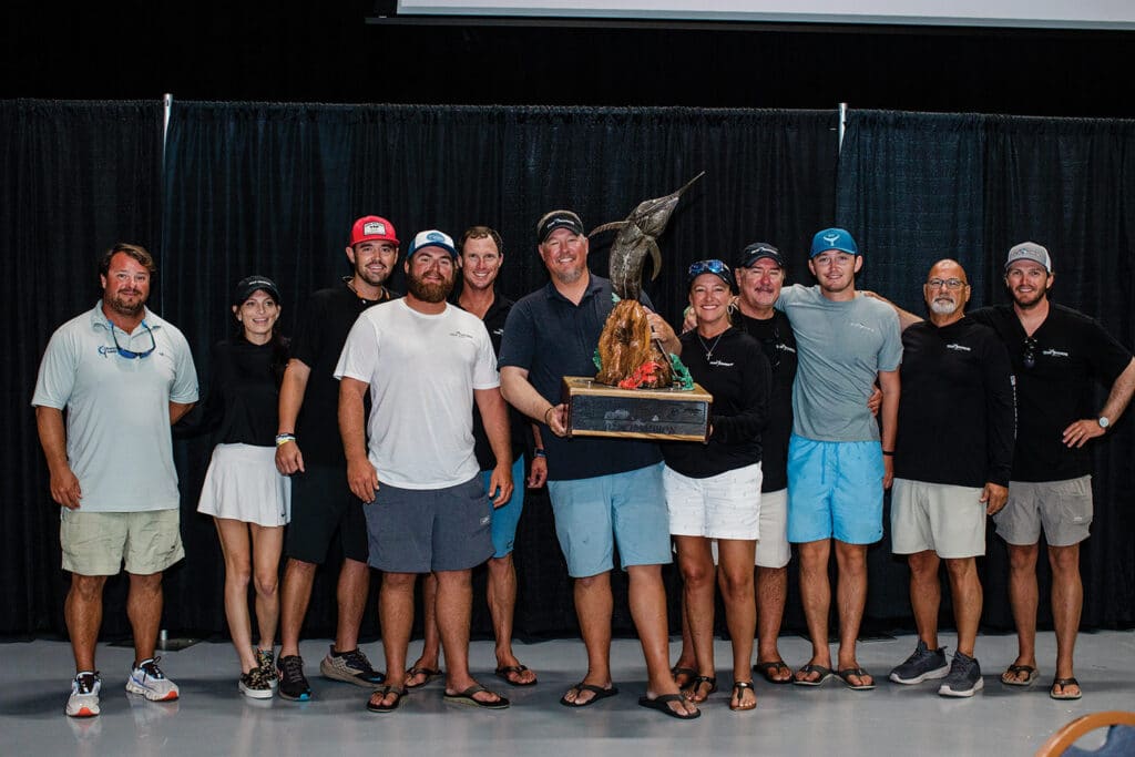 A sport-fishing team of 11 stand together and pose, while the center crew holds up a large trophy.