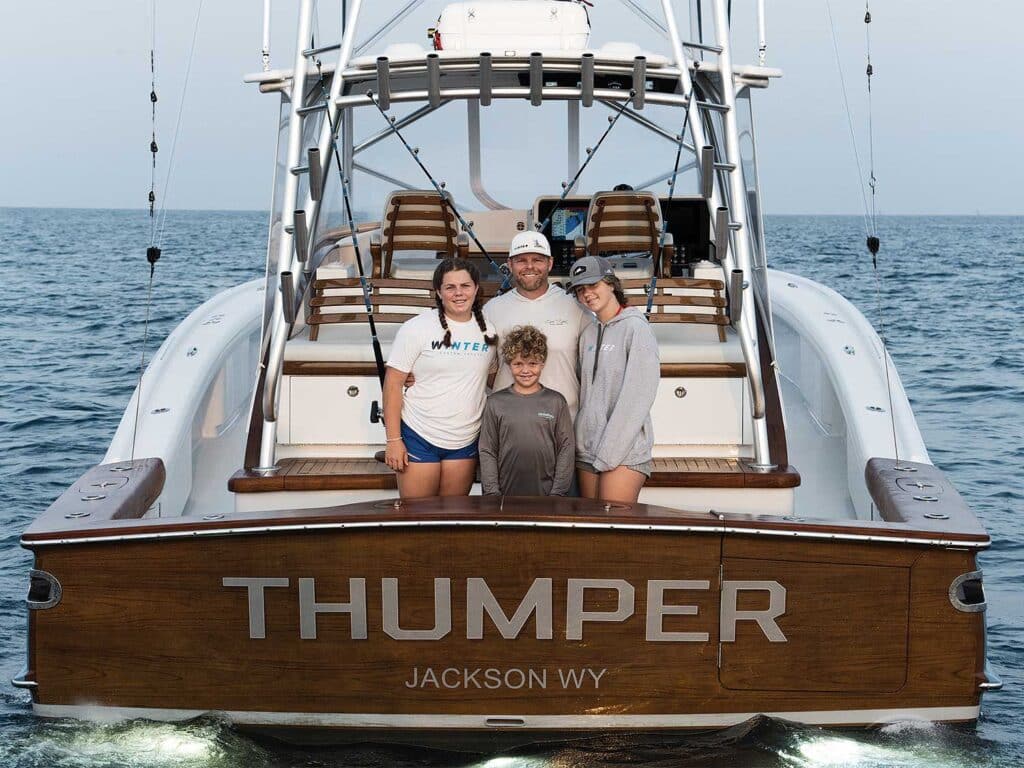 A family of four stand in the cockpit of a center console sport-fishing boat.