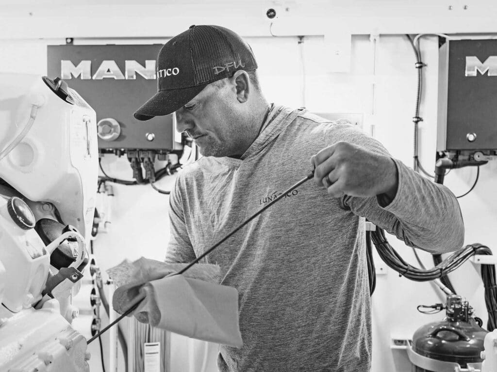 Black and white image of a man checking the engine of a sport-fishing boat.