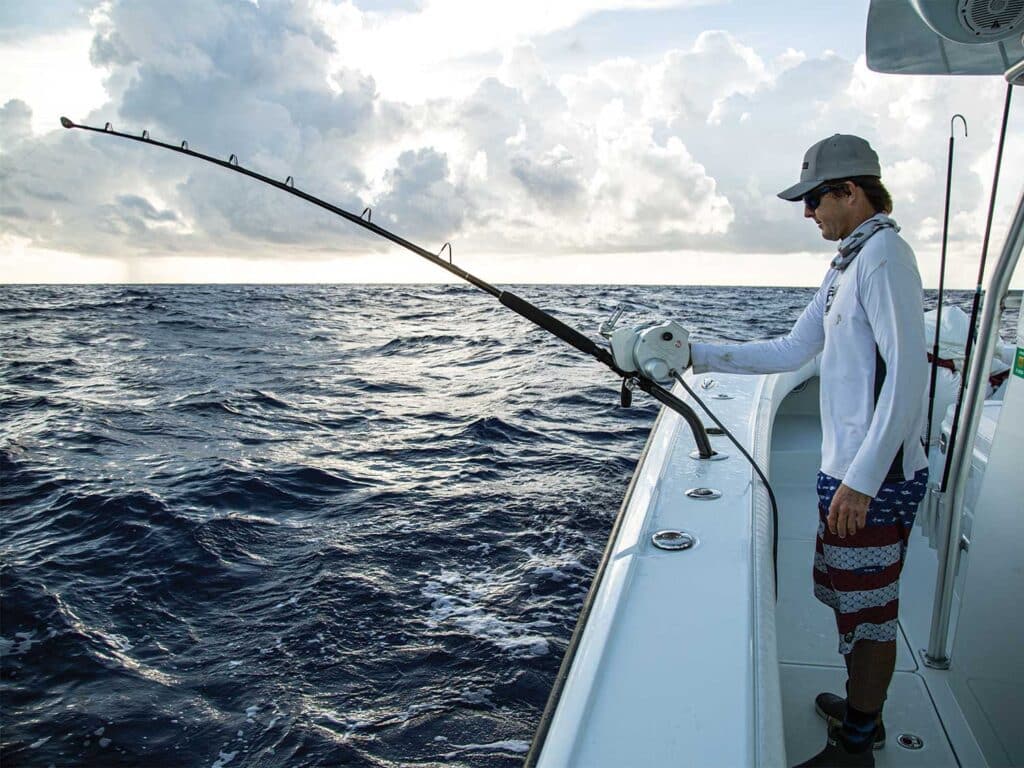 A sport-fishing angler stands in the cockpit, overlook tackle and the ocean.