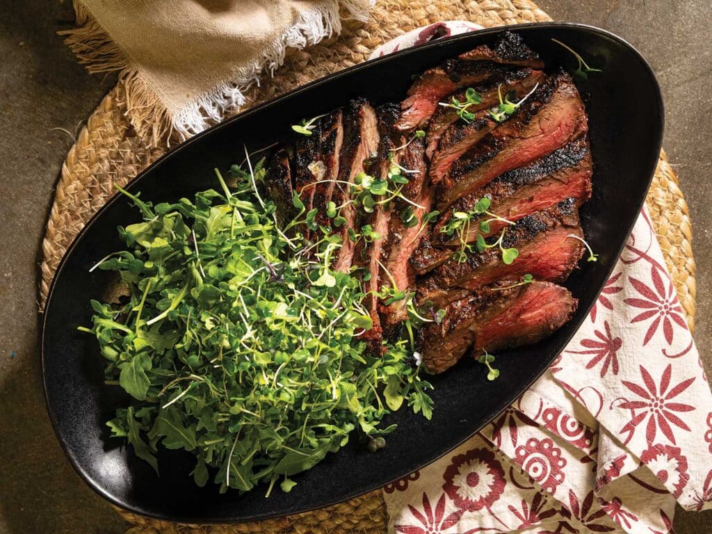 Grilled Rib-Eye Cap Steak with Peri Peri Sauce in a bowl and topped with fresh herbs and a side arugula salad.