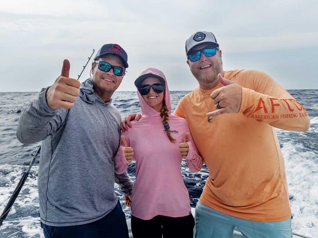 Three sport-fishing anglers stand in the cockpit and pose for a photo.