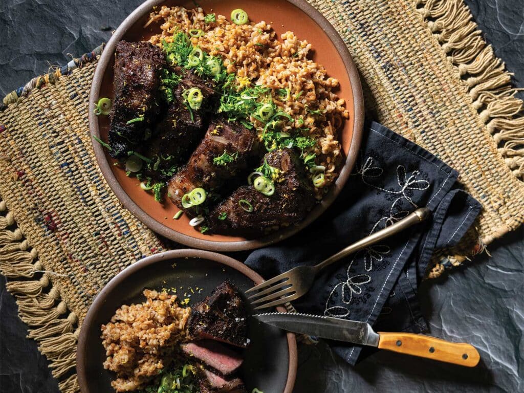 Sumac and Red Wine Lamb Chops with Bulgur Pilaf and Spring Onion Salad , served in a bowl and garnished with freshly chopped green onions.