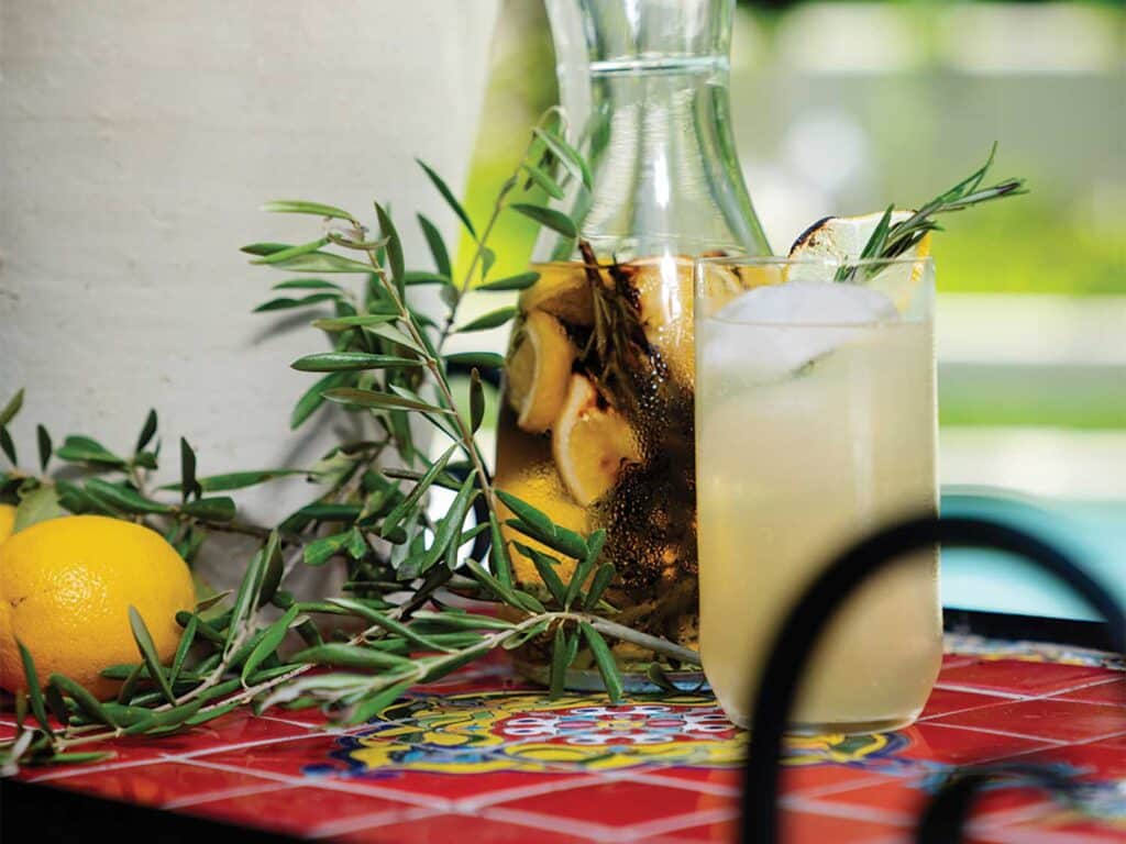 Tito's Charred Vinyl cocktail served in a glass and garnished with sprigs of rosemary and slices of lemon.