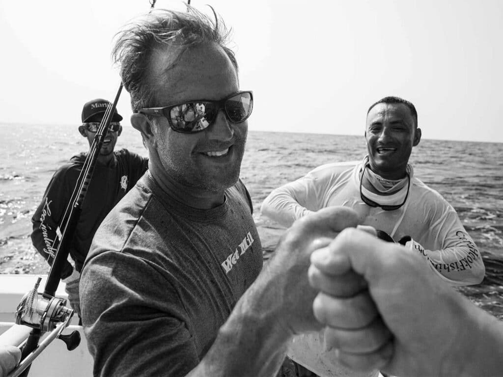 A black and white image of three sport-fishing anglers cheering each other on in the cockpit of a sport-fishing boat.