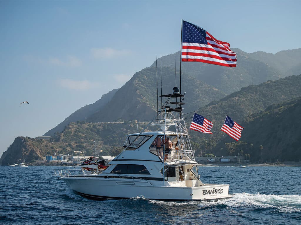 A sport-fishing boat flying American flags leads a fleet of boats out to sea.