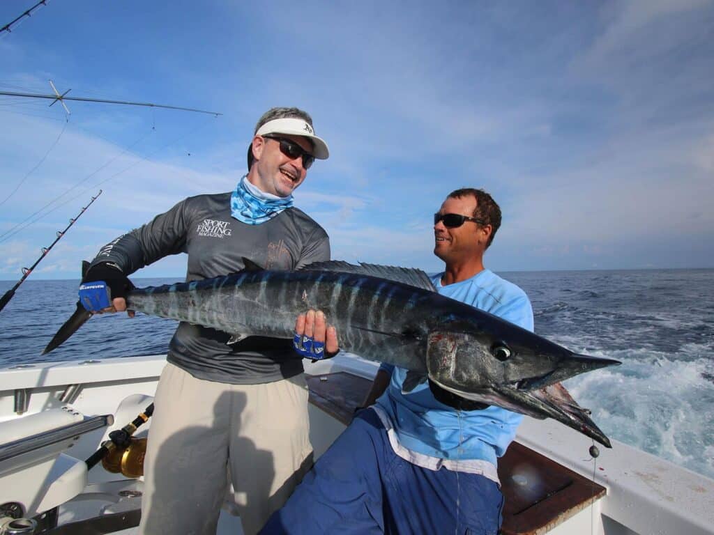 Two sport-fishing anglers pull a large wahoo aboard.