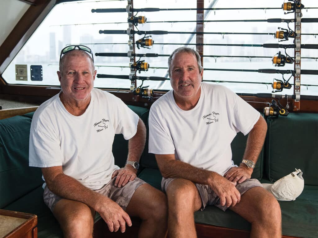 Two men sitting in the salon of their sport-fishing boat, with fishing reels and rods in the backdrop.