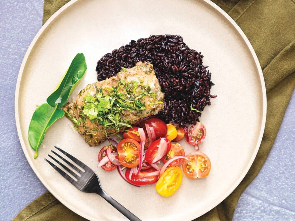 A plate of green curried snapper over a bed of black rice.