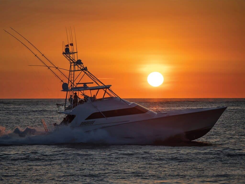 A sport-fishing boat cruises across the ocean at sunset.