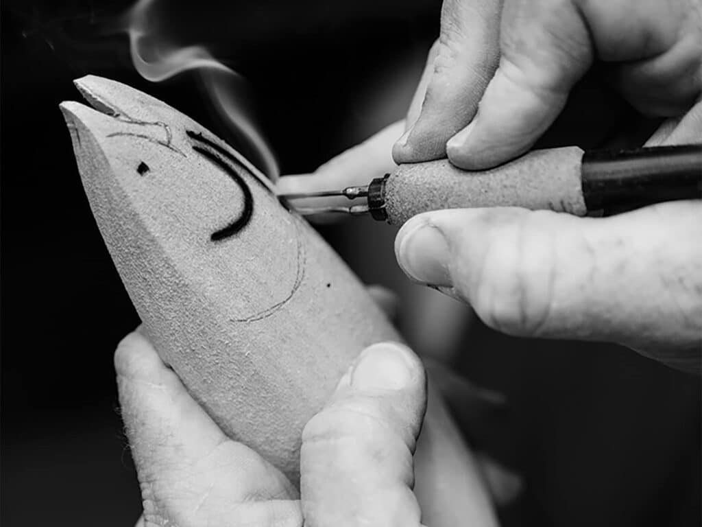 A black and white image of Chris Costello applying wood-burn details on a fish trophy.