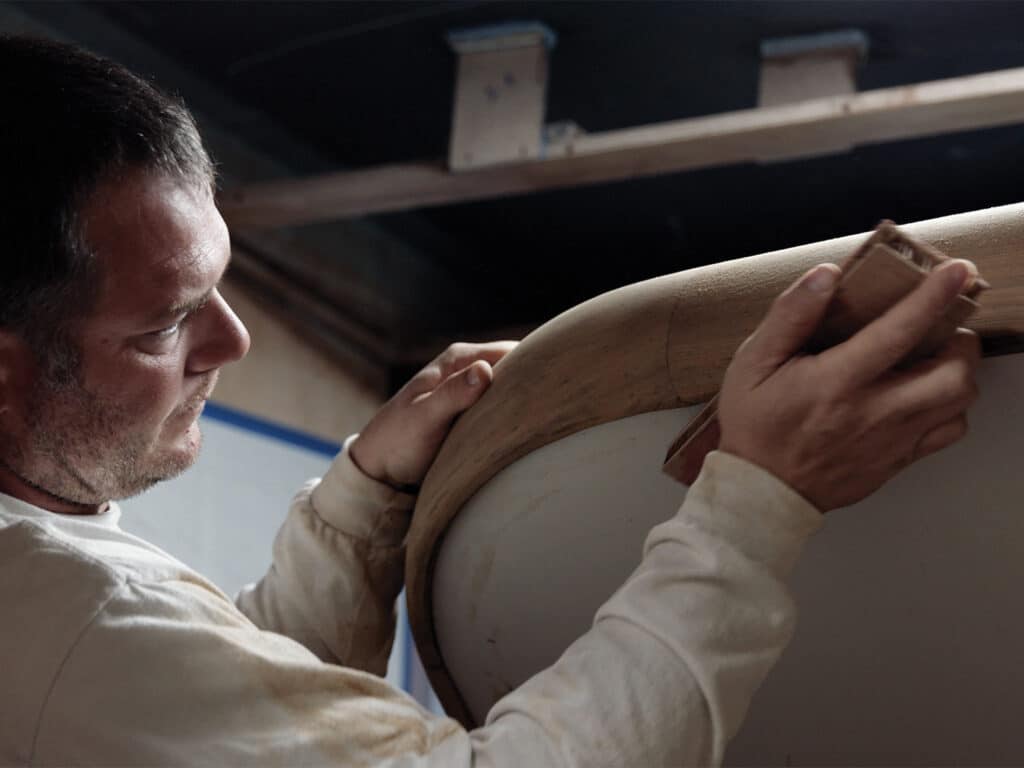 A boat builder doing detail work on wood finishes for a boat.