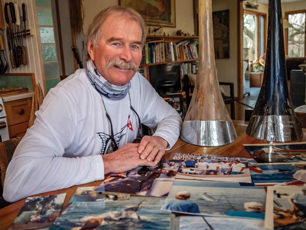 Charles Perry at his table next two two billfish trophies and dozens of photographs on the table in front of him.