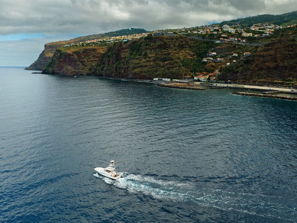 A sport-fishing boat cruises along the coast of Madeira on calm waters.