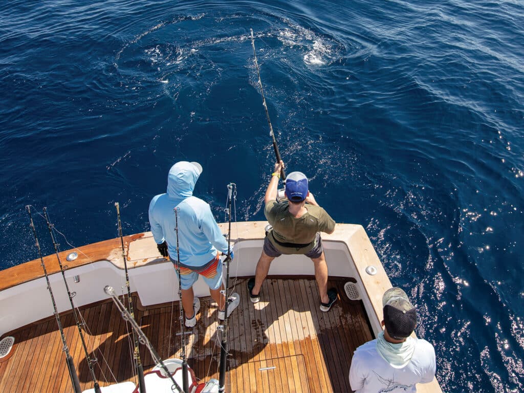 View of the cockpit from the tower, where several anglers reel a marlin in boatside.