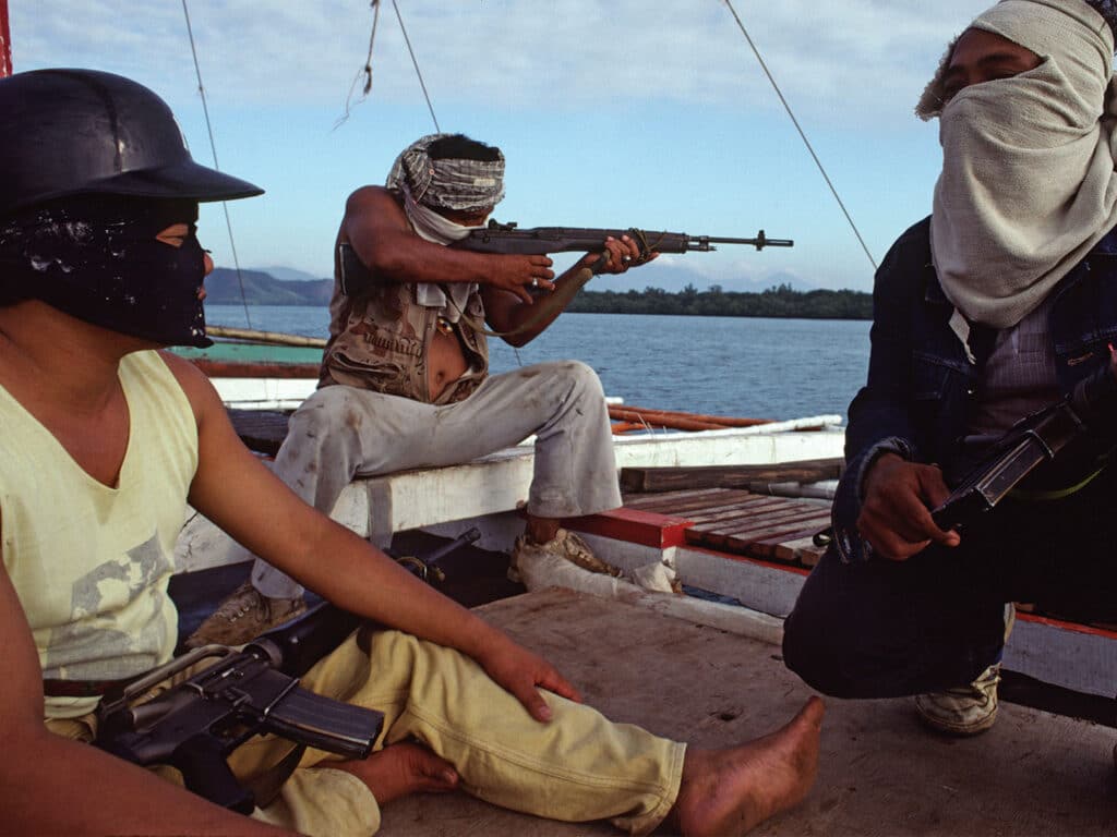 Three men with guns and face coverings on a boat dock.