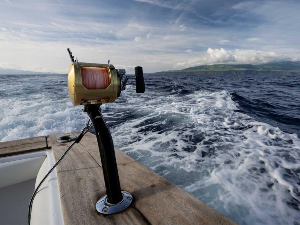 A sport-fishing reel nestled into the cockpit's holders on a sport-fishing boat, overlooking the ocean and distant horizon.