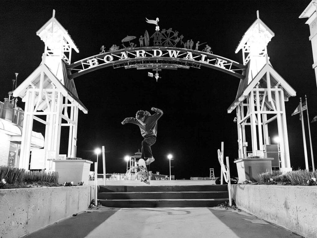 Black and white image of a skateboarder mid-jump in front of the iconic Ocean City, Maryland Boardwalk sign.