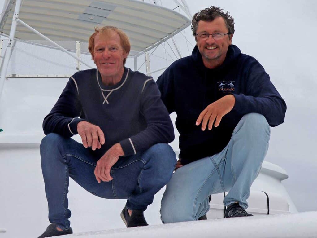 Two men kneel and post on the deck of a sport-fishing boat.