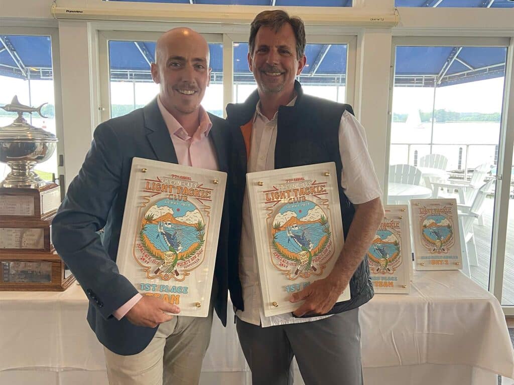 Two anglers at an awards ceremony holding up plaques.