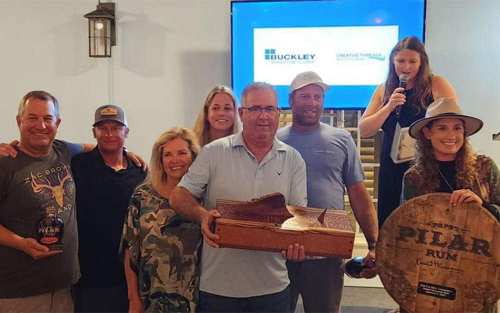 Seven angelrs stand at an awards ceremony and hold up sport-fishing trophies and awards.