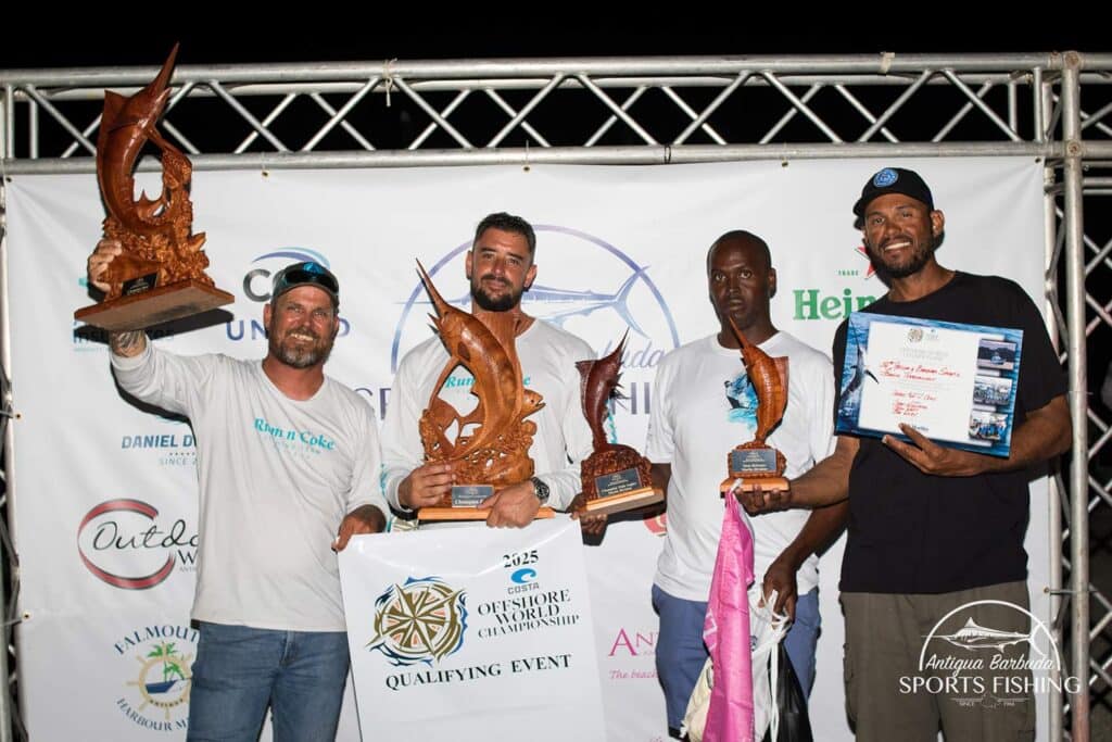 Four anglers hold up carved wooden trophies and prizes at a sport-fishing tournament ceremony.