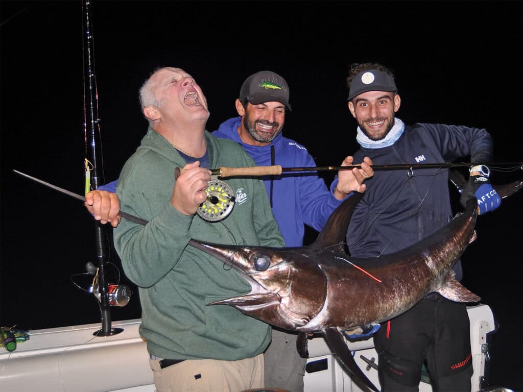 Three anglers holding up a swordfish after being caught on the fly.