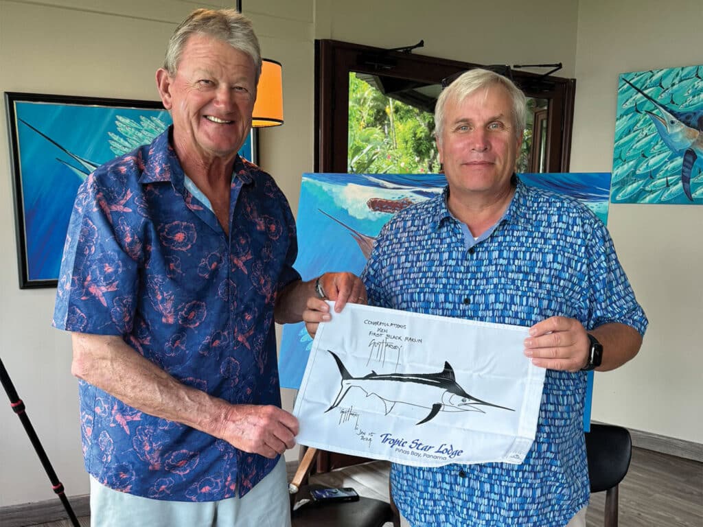 Two men holding up a black marlin flag.