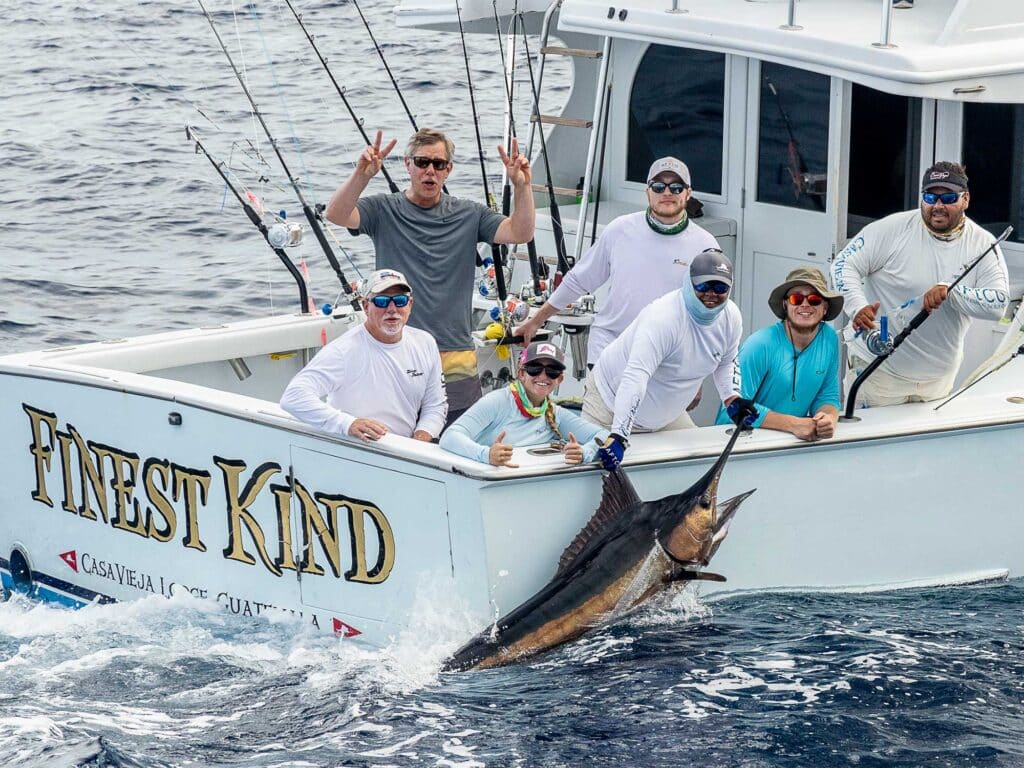 A sport-fishing team holds a marlin boatside for a photo before release.