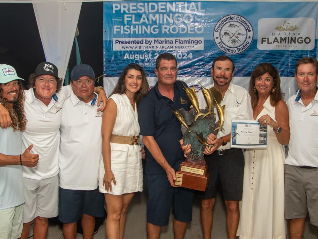 Anglers standing at an awards ceremony. The center angler is holding up a large wood and bronze trophy.
