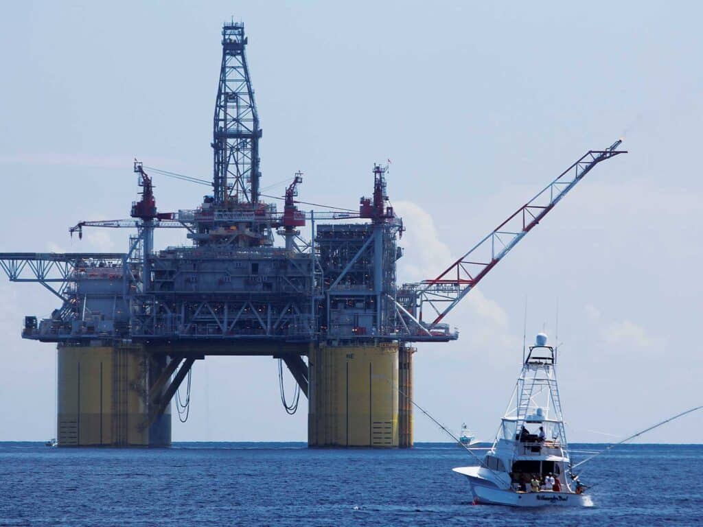 A sport-fishing boat cruising near an oil rig on the water.