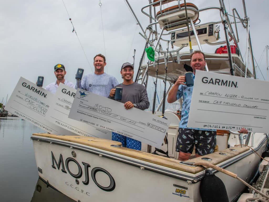 A group of anglers standing in the cockpit of a sport-fishing boat and holding up oversized checks.