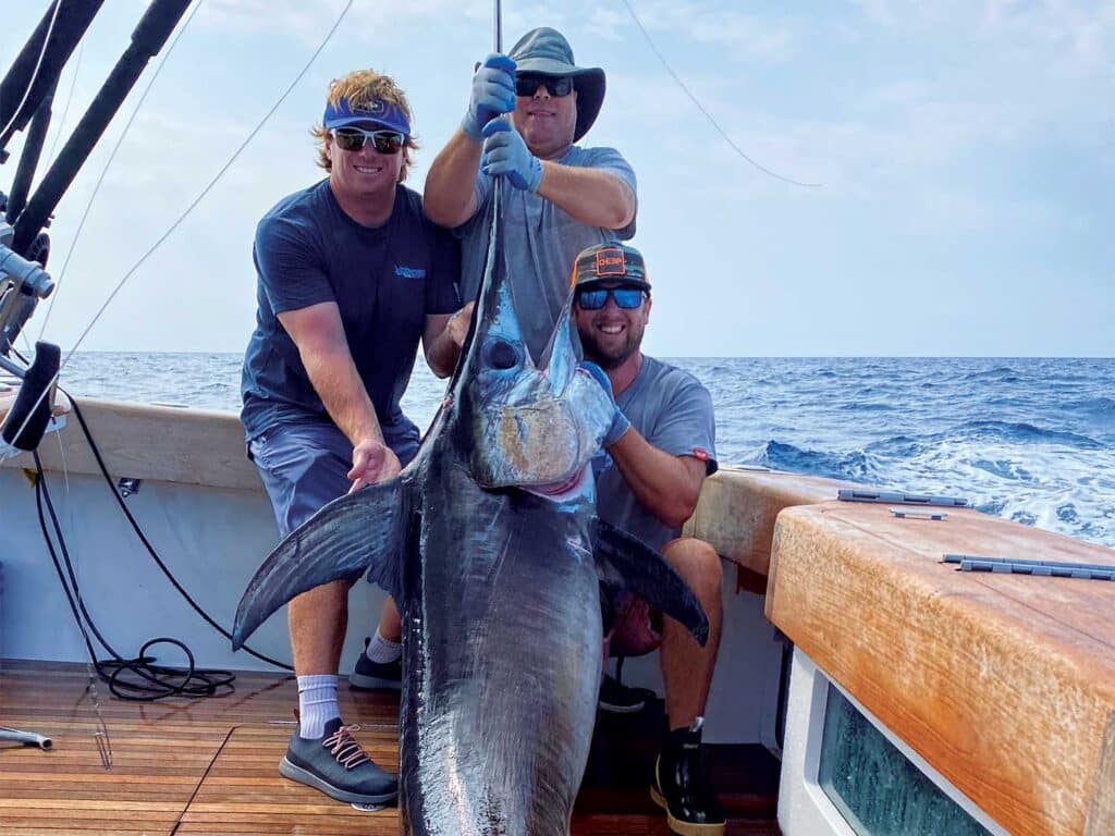 Three angelrs holding up a swordfish.