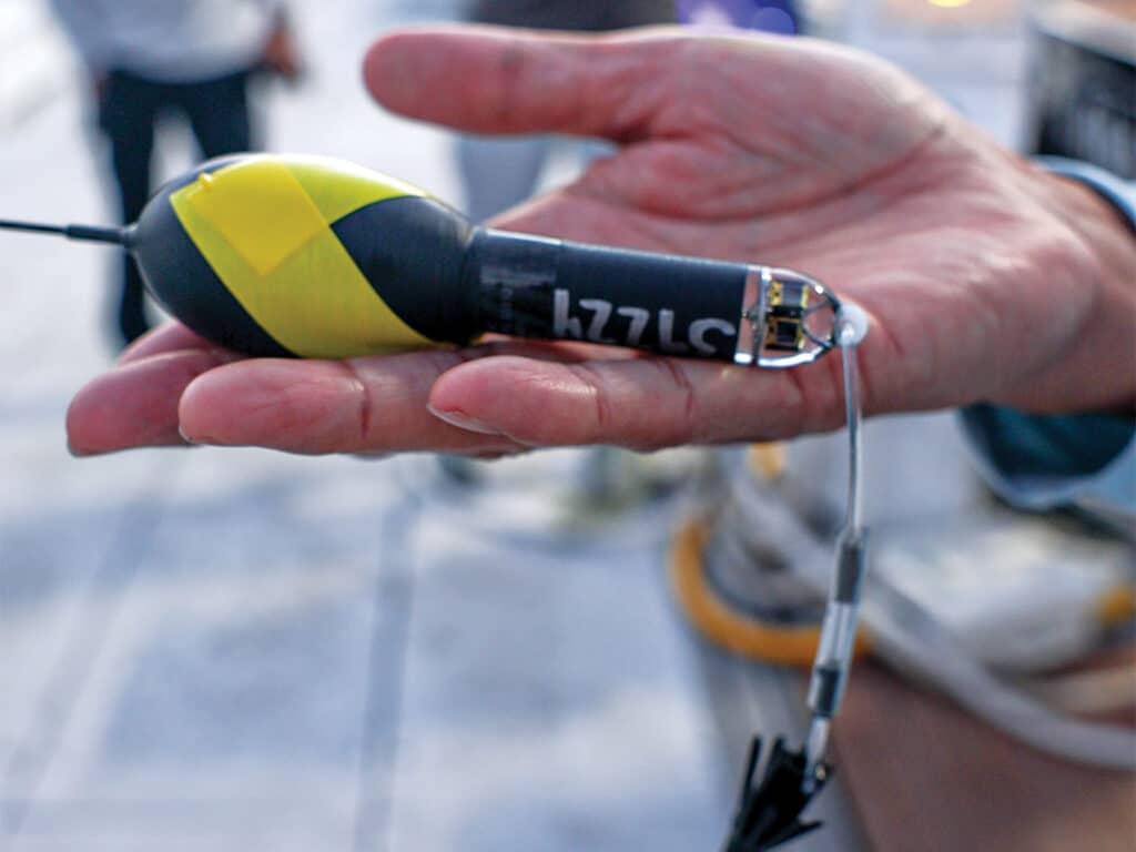 Close up detail of a satellite tag being held in the palm of an angler's hand.