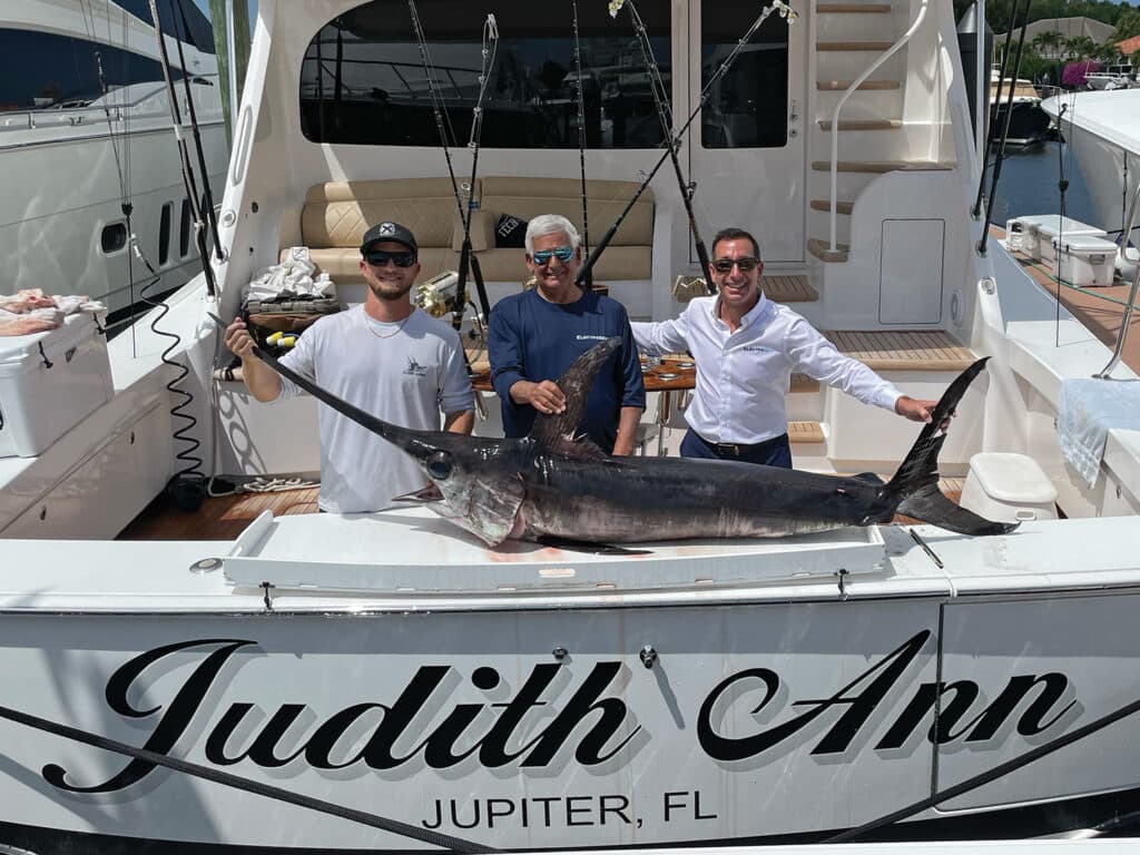 Three anglers stand in the cockpit of a sport-fishing boat.