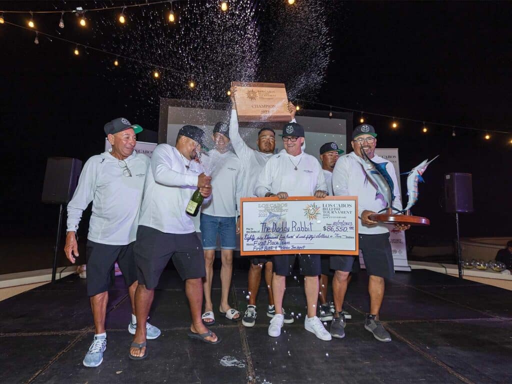 Team The Daddy Rabbit at the 2023 Los Cabos Billfish Tournament. They stand holding champagne bottles spewing beverage in the air. They also hold an oversized check.