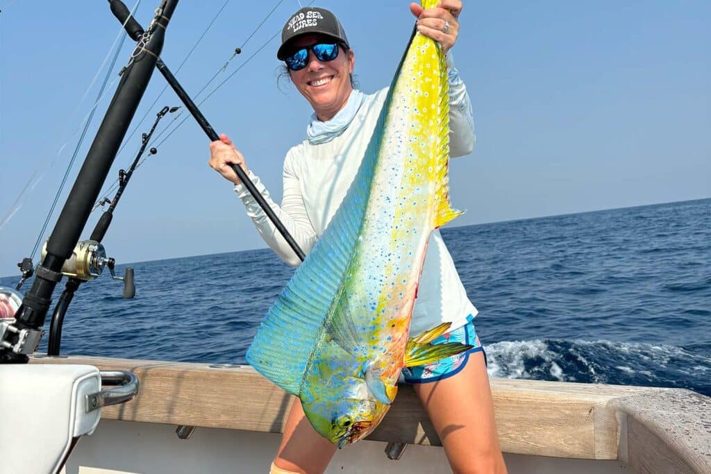 A woman angler stands in the cockpit of a sport-fishing boat and holds up her dorado.