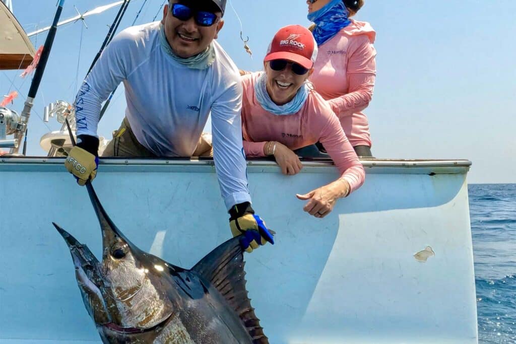 A crew and anglers pull a marlin boatside.