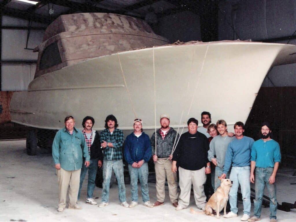 A crew of boat builders standing next to an unfinished boat hull.