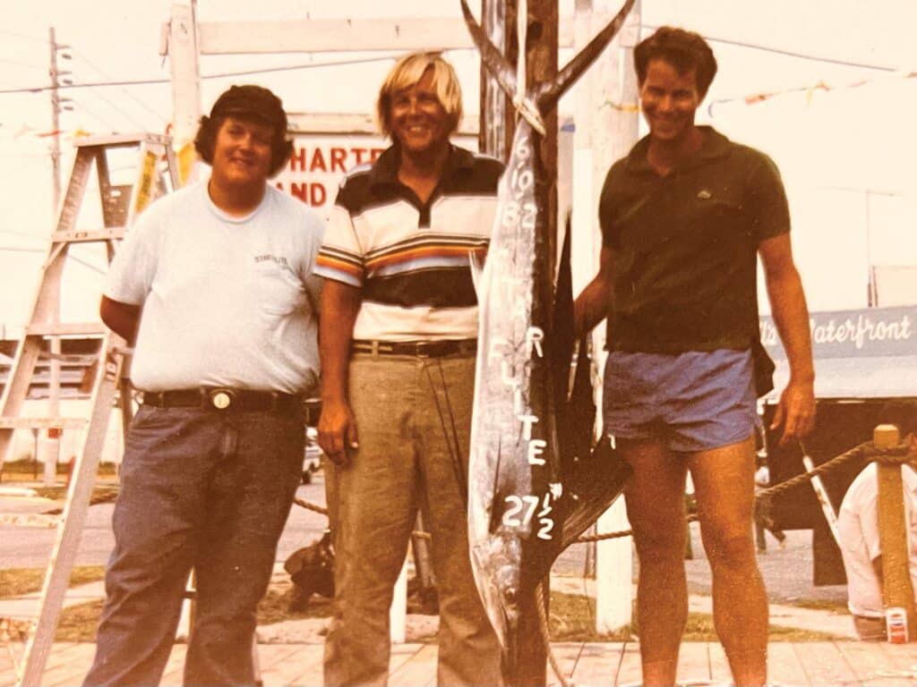 Three men standing by a fish.