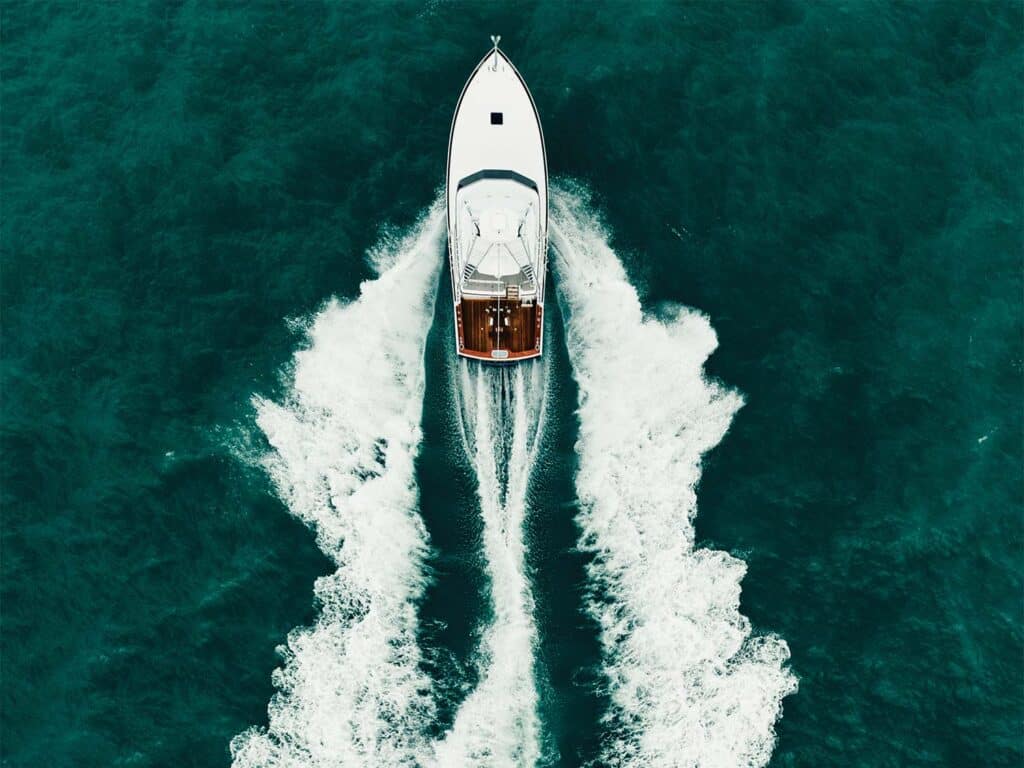 Top-down aerial view of a sport-fishing boat cruising across the water, leaving cresting waves in its wake.