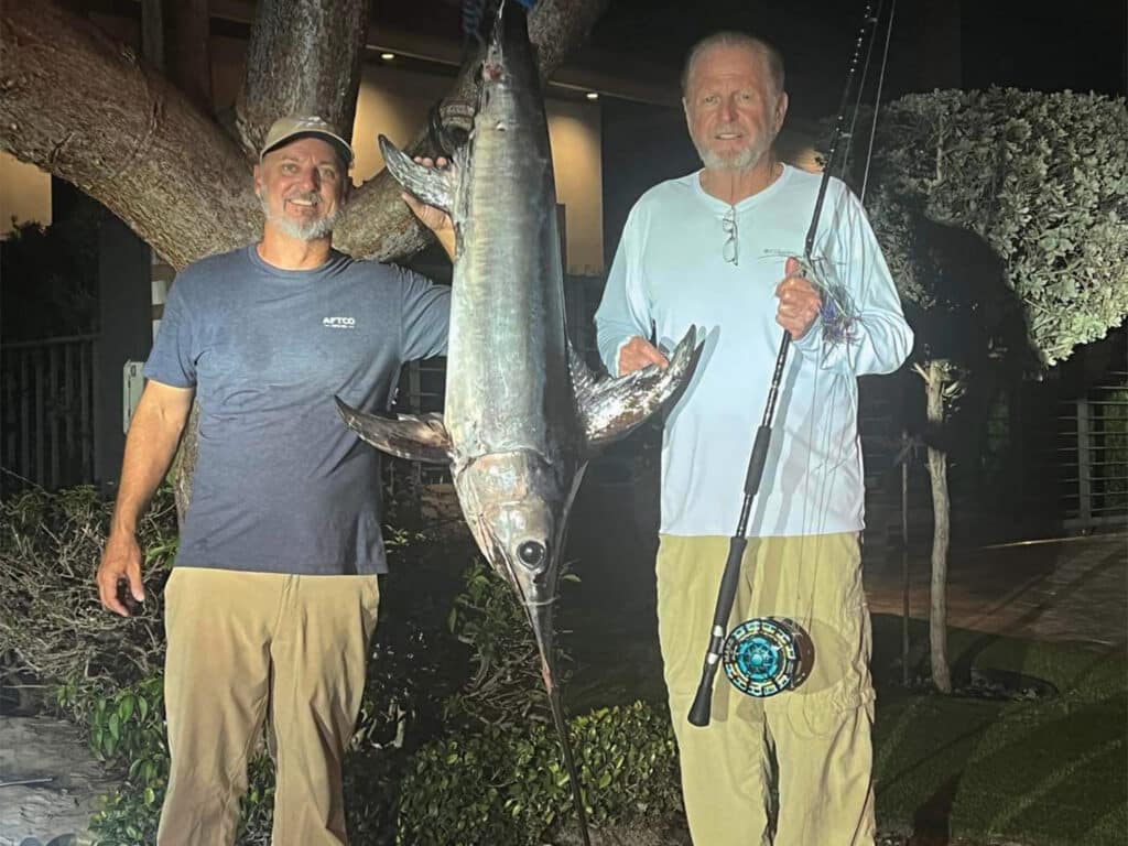 Two men standing on either side of a swordfish.