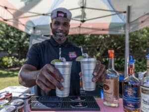 A bartender holding up two stainless steel glasses of cocktails garnished with lime.