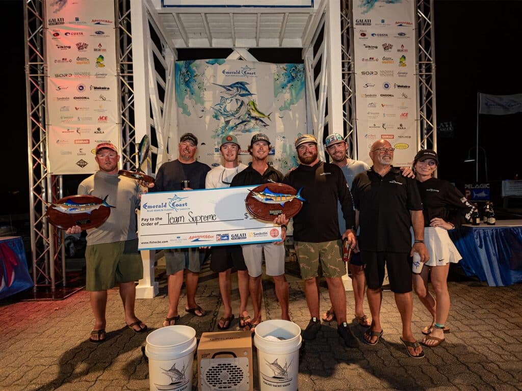 A sport-fishing team celebrates at the Emerald Coast Blue Marlin Classic awards ceremony. They hold up an oversided check