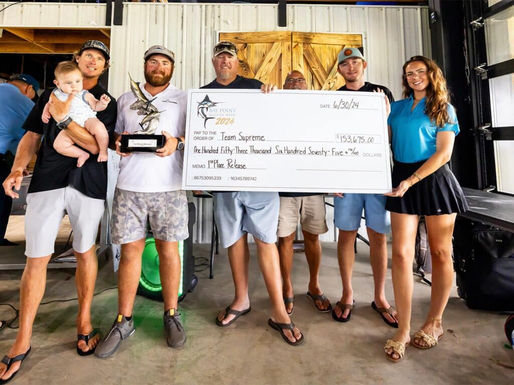 Team Supreme stands in celebration at an awards ceremony. They hold up trophy prizes and an over-sized check.