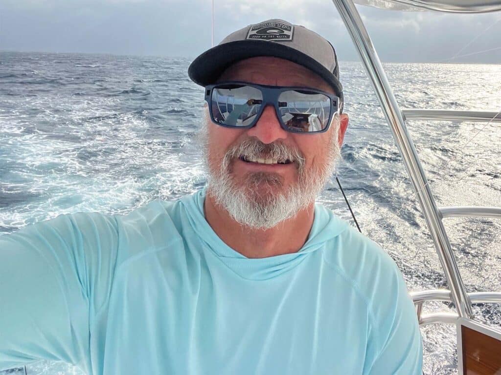 Capt. Tim Richardson wearing sunglasses and a cap stands at the helm.