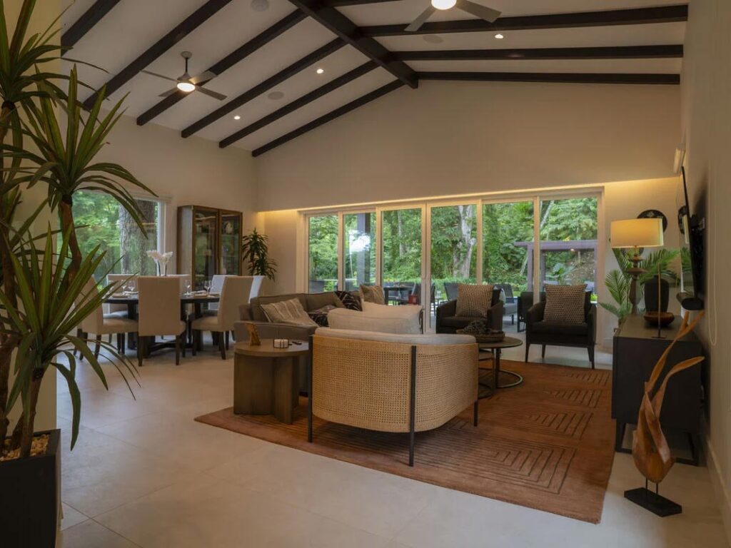 View of the interior of a Casa Selva Tica dwelling. Glass windows cover the side of a wall showing the vibrant, lush outdoors beyond.
