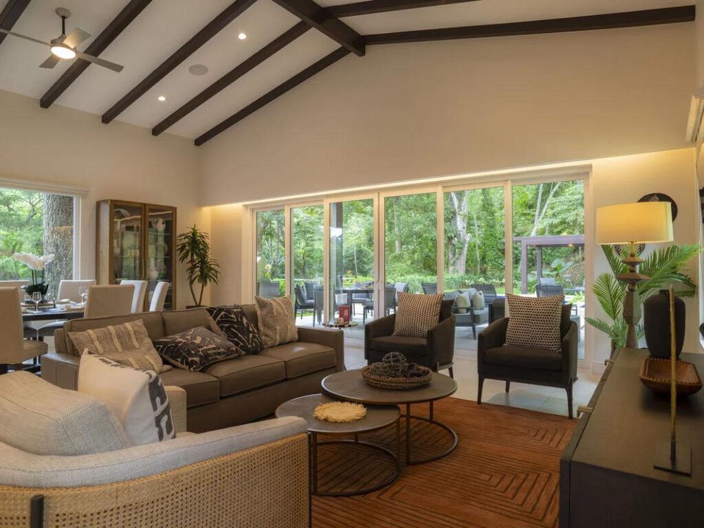 View of the interior of a Casa Selva Tica dwelling. Glass windows cover the side of a wall showing the vibrant, lush outdoors beyond.